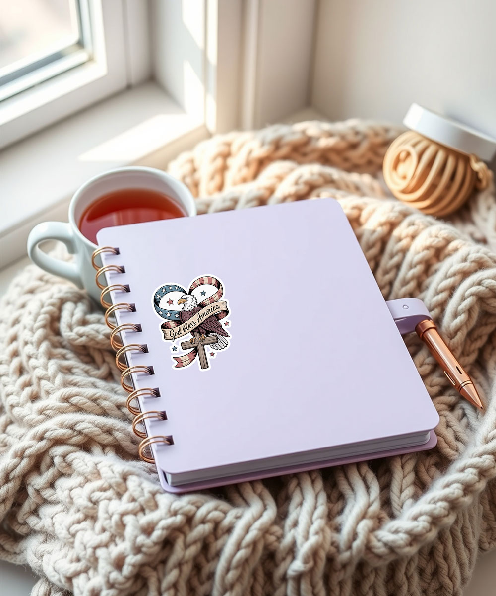 "God Bless America" design Christian sticker on a light purple notebook, with a knitted blanket and pen.