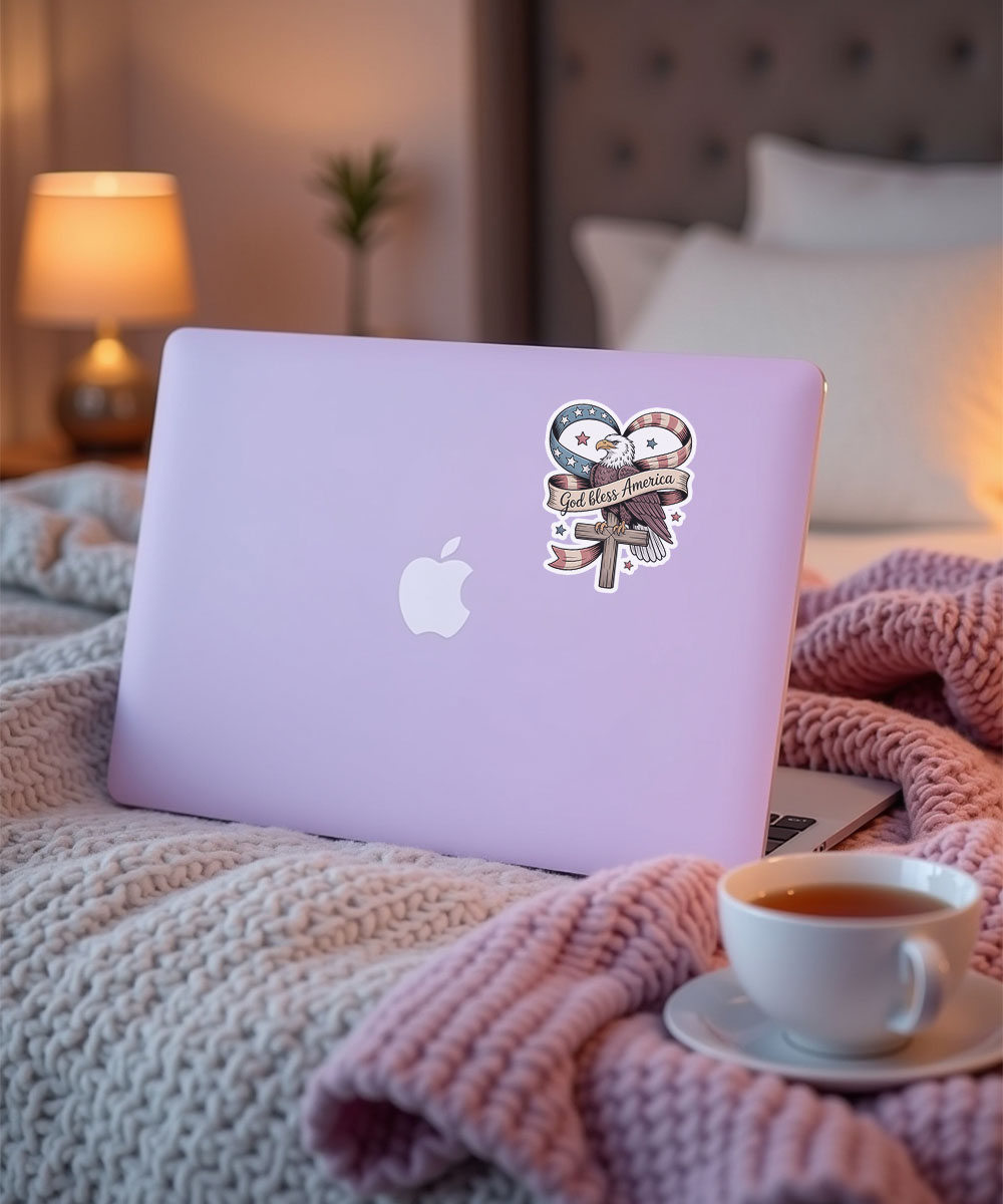 god-bless-america-bible-verse-sticker-on-laptop Christian faith sticker with the quote "God Bless America" applied to a purple laptop in a cozy setting.
