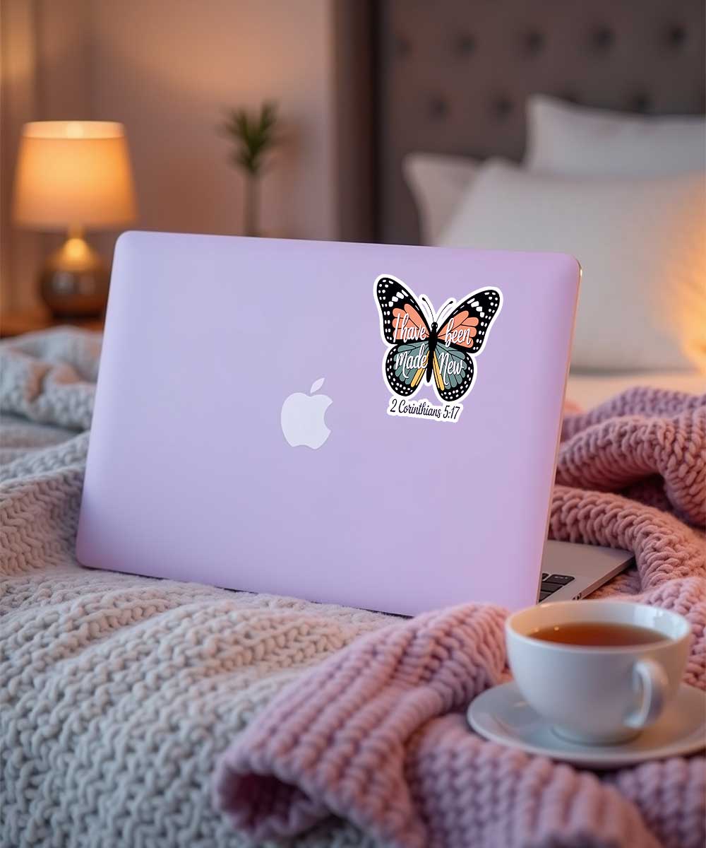 i-have-been-made-new-bible-verse-sticker-on-laptop Christian faith sticker with the quote "I have been made New 2 Corinthians 5:17" applied to a purple laptop in a cozy setting.