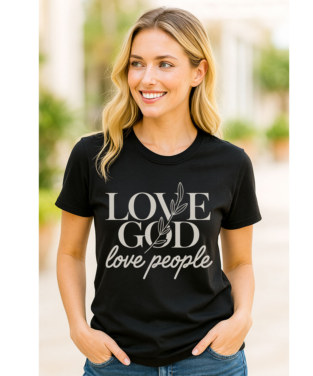 A smiling woman with blonde hair who appears to be Caucasian models the black "Love God Love People Christian T-Shirt" outdoors.