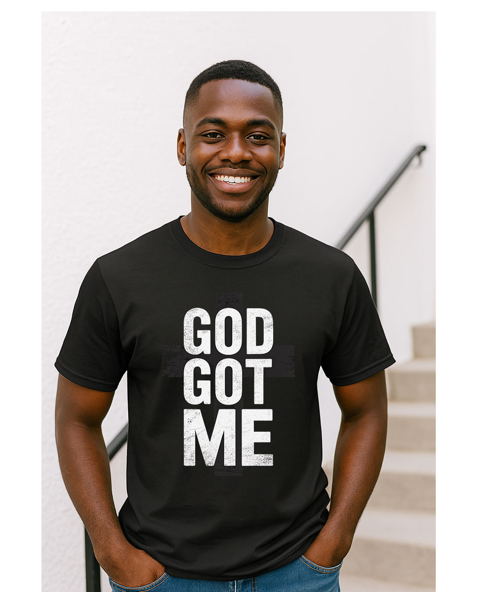 A smiling man who appears to be Black models the "God Got Me Christian T-Shirt" outdoors.