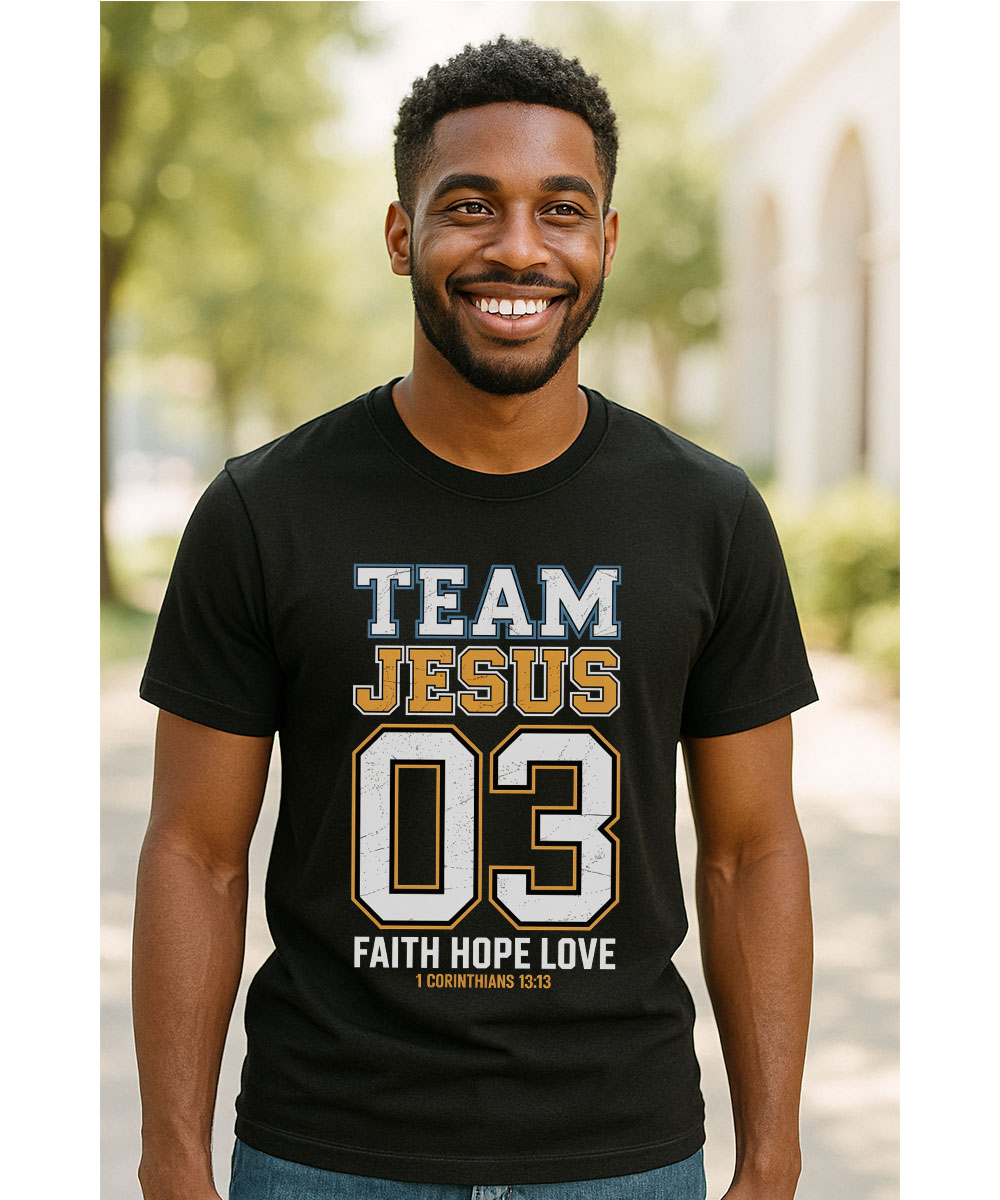 A smiling man who appears to be Black wears the men's "Team Jesus T-Shirt" in black, featuring the Faith Hope Love design.