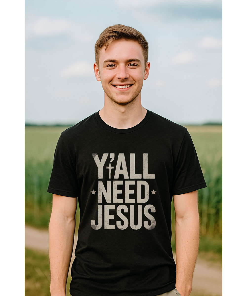 A smiling young man who appears to be Caucasian models the "Y'all Need Jesus Christian T-Shirt" outdoors in a field.
