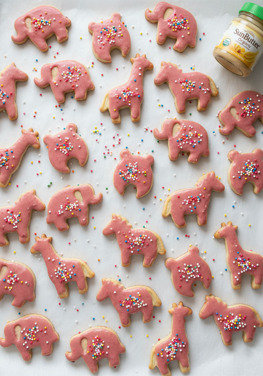 Overhead flat lay of homemade dairy-free frosted animal crackers with pink glaze and rainbow sprinkles on parchment paper