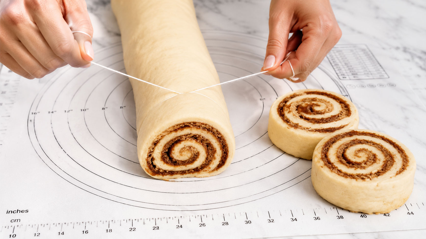 Slicing a vegan cinnamon roll log into individual rolls using dental floss showing perfect cinnamon spirals